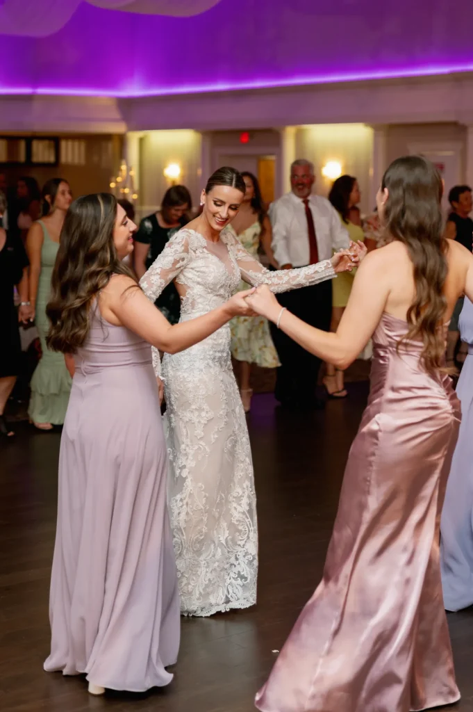 Bride dancing with two bridesmaids on the dance floor with wedding guests in the background at Croatian Lodge
