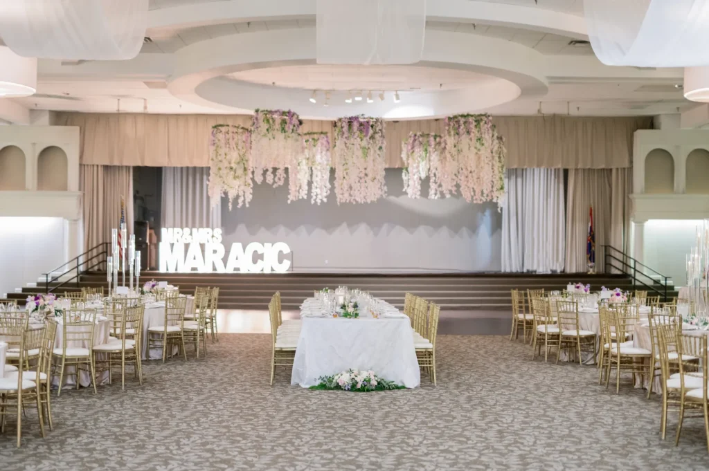 Wide view of a decorated wedding hall at Croatian Lodge, showing tables and floral ceiling decorations, with a newlyweds' sign in the background